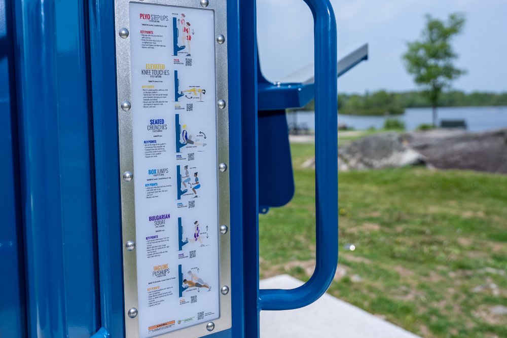 Instructional placard mounted on Outdoor-Fit outdoor fitness equipment showing exercise guidance and proper usage instructions.